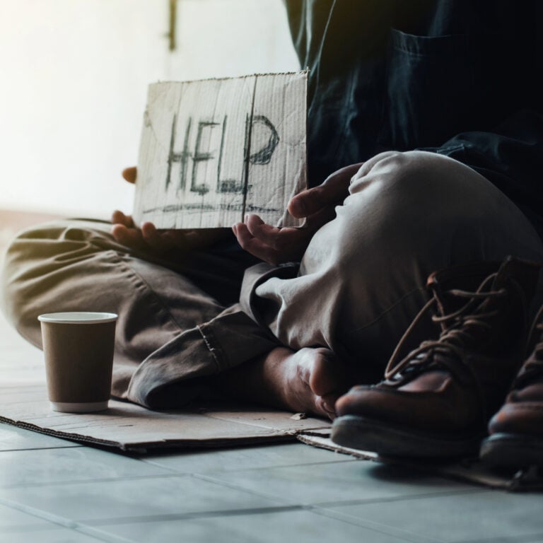 Person sitting on the ground holding a cardboard sign reading “HELP” to highlight homelessness crisis