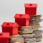 Red model houses stacked on coins representing property investment and rental market finances