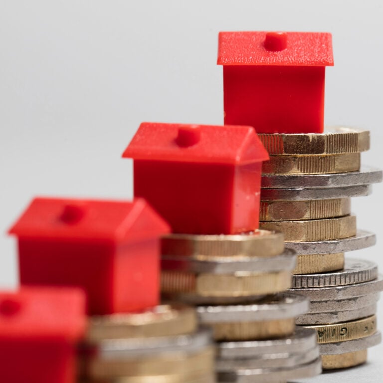 Red model houses stacked on coins representing property investment and rental market finances