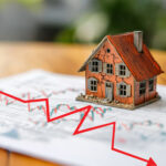 Cracked model house beside falling market chart illustrating weakening UK housing activity
