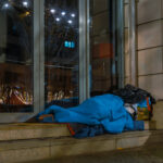 Person sleeping rough on a city doorstep at night, highlighting the urgency of homelessness prevention measures.