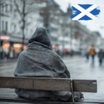 Person wrapped in a blanket sitting alone on a bench during cold, wet weather in Scotland