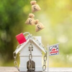 House model chained with padlock and falling money bags illustrating social housing affordability pressures