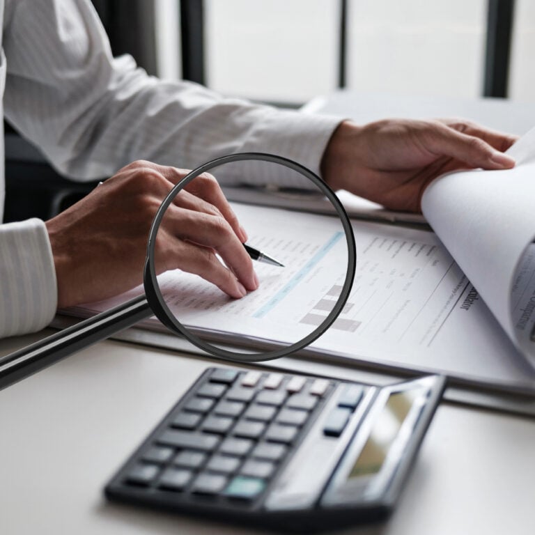 Person reviewing housing benefit figures with a magnifying glass, paperwork and calculator on desk