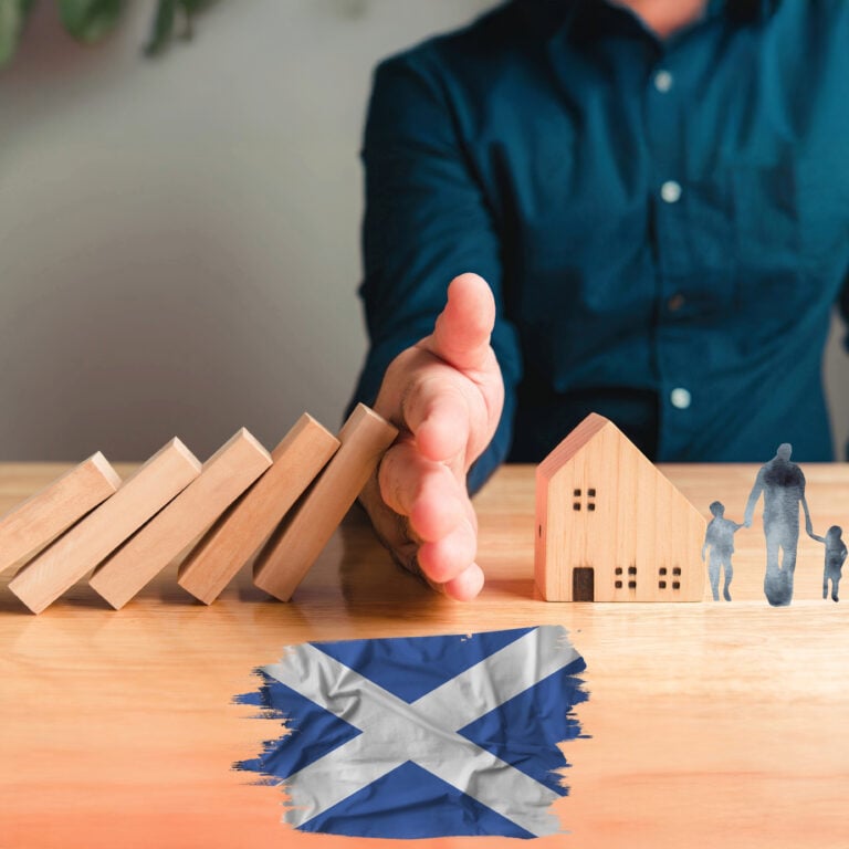 Hand stopping falling blocks beside a wooden house and family figures, symbolising protecting domestic abuse victims’ housing in Scotland