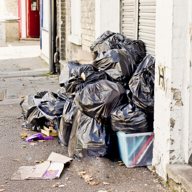 Piles of black rubbish bags left on a residential pavement, highlighting fly-tipping and improper waste disposal.