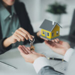 Landlord hands over buy-to-let property keys beside a model house during a rental transaction