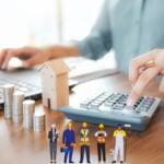 Landlord calculating rental property running costs with calculator, coins, and house model