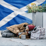 Homeless man sleeping on pavement in Glasgow with Scottish flag in background
