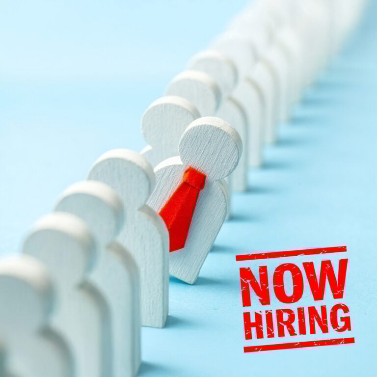 Wooden figures in a line with one highlighted in a red tie and a “Now Hiring” stamp