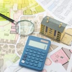 Model house, calculator and magnifying glass on planning maps illustrating UK housing development and costs