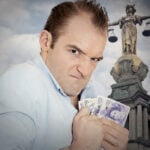 Man clutching cash in front of Lady Justice statue, symbolising alleged landlord overcharging