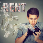 Frustrated renter looking into empty wallet as cash falls around him beneath “Rent” headline