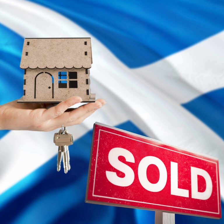 Hand holding model house and keys with sold sign against Scottish flag backdrop