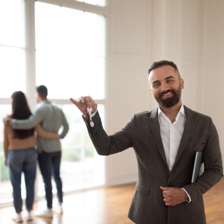 Estate agent holding house keys while a couple stands together in their new home during a property sale