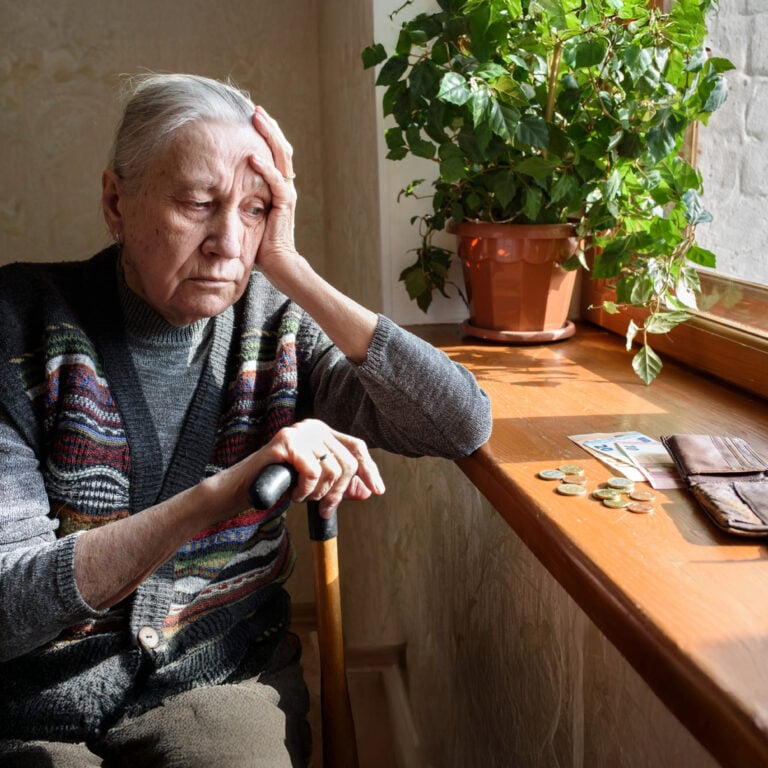 Worried elderly woman with a walking stick looking at cash on a table, illustrating pensioner poverty and housing costs