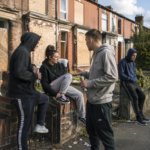 Group of young people outside boarded-up homes, illustrating anti-social behaviour in a residential neighbourhood.
